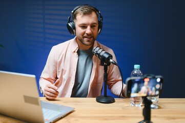 Man podcaster influencer blogger smiling while broadcasting his live audio podcast in studio using...
