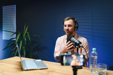 A video blogger records content in his studio. The host of the video blog is a young man who is...