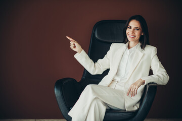 Beautiful businesswoman pointing with a gesture seated in a modern black chair against a brown...