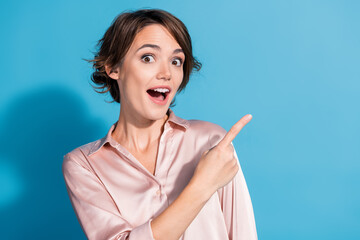 A young woman with a charming smile pointing with surprise and delight on a vibrant blue background