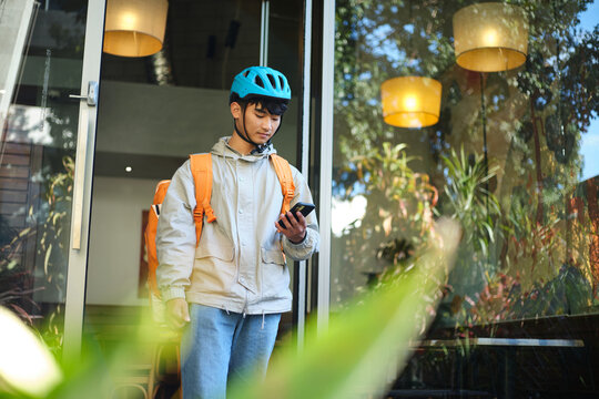 Asian delivery guy walking out of the restaurant while on his phone.