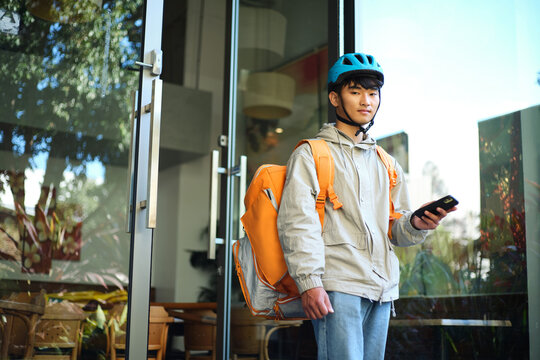Asian delivery guy walking out of the restaurant while on his phone