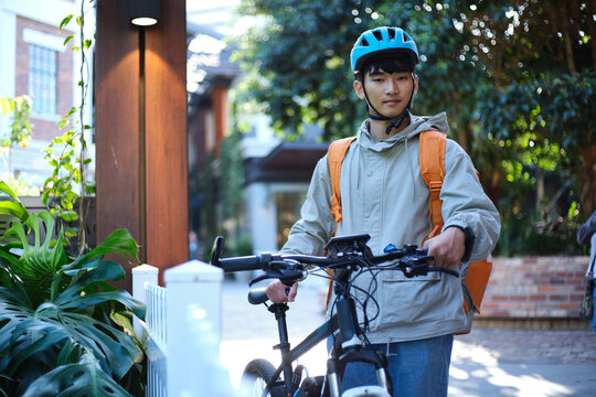 Asian delivery boy walking with his bicycle.
