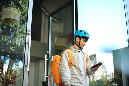 Asian delivery guy walking out of the restaurant while on his phone.