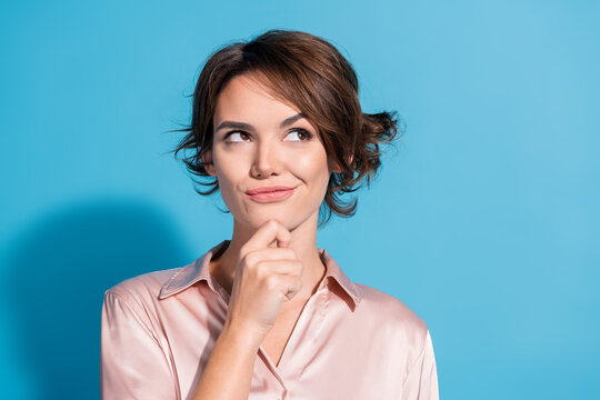 Confident young woman in satin pink blouse showcasing a thoughtful expression against a vibrant blue backdrop