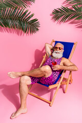Photo of cheerful nice retired man wear swimwear relax rest chaise lounge enjoy resort isolated on pink color background