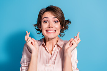 Young woman joyfully crossing her fingers for good luck in a stylish pink blouse against a vibrant...
