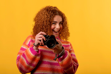 Obraz premium Enthusiastic photographer smiling and holding a camera in studio with yellow background