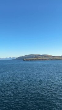 Rocky coastline and island in the Faroe Islands surrounded by deep blue ocean under a clear sky. Tranquil and remote seascape of the North Atlantic.