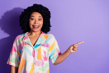 Cheerful young woman in colorful shirt showing with finger against violet background