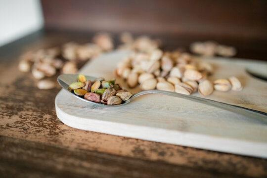 Shelled pistachios on a metal spoon with whole nuts in background