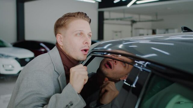 Young man strokes car door expressing owner adoring in dealership