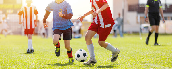 Exciting Youth Soccer Match: Young Players Compete for the Ball Under Sunny Skies on a Green Grass Field. Kids Soccer Game in Full Swing: Young Players Competing for Ball on Sunny Day with Referee