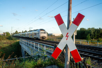 Andreaskreuz an elektrifiziertem Bahnübergang mit fahrendem Zug