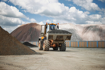 Heavy machinery moves gravel in a construction site with mountains of material under a cloudy sky