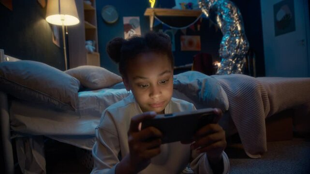 Little Black girl in pyjamas sitting on floor in dark room at night absorbed into smartphone screen while mysterious alien creature sneaking in room looking for something then walking away unnoticed