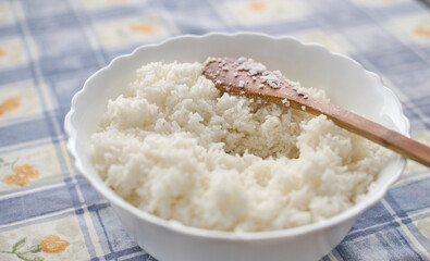 Large bowl filled with freshly boiled white rice cooling down with a wooden spoon for mixing, before being used in fried rice recipes.