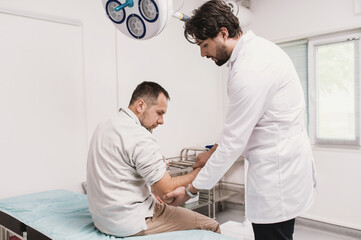 Obraz premium traumatologist examines male patient's elbow in hospital on couch in emergency room. range of motion test, pain, arm injury. Arthritis and joint problems, arthrosis, bruise, broken arm vertical