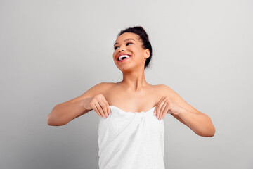 Smiling young woman wrapped in towel against neutral background, enjoying fresh and radiant feeling