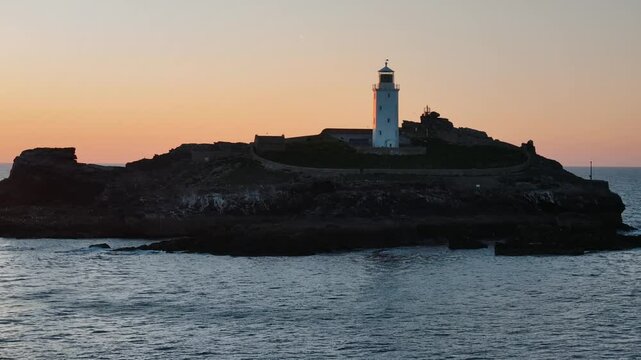 Drone ascends toward Godfrey&rsquo;s Point Lighthouse at dusk, revealing silhouette against glowing sky, establishing backdrop