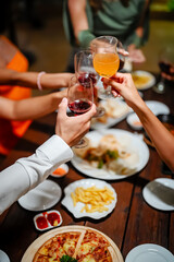 Close-up of friends sharing a delicious meal and drinks at a lively dinner party, featuring seafood, fries, and wine on a wooden table