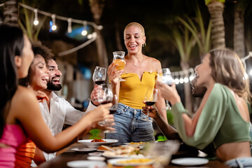 Group of diverse friends raising glasses in a joyful toast at a tropical outdoor party, celebrating together under palm trees and string lights