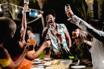 Group of diverse friends raising glasses in a joyful toast at a tropical outdoor party, celebrating together under palm trees and string lights