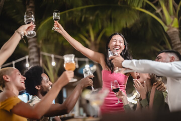 Group of diverse friends raising glasses in a joyful toast at a tropical outdoor party, celebrating together under palm trees and string lights