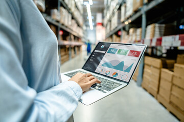 Employee using a laptop with business analytics dashboard in a modern warehouse, showing real-time...