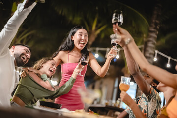 Group of diverse friends raising glasses in a joyful toast at a tropical outdoor party, celebrating together under palm trees and string lights