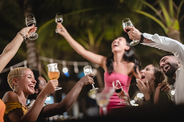 Group of diverse friends raising glasses in a joyful toast at a tropical outdoor party, celebrating together under palm trees and string lights