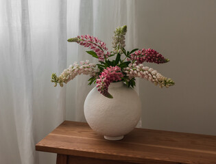 Bouquet of lupines in a round ceramic vase on a wooden bench