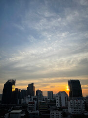 Obraz premium A city skyline at sunset with tall buildings silhouetted against a colorful sky filled with scattered clouds.