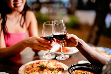 Romantic couple enjoying a dinner date at an outdoor restaurant, toasting with red wine, smiling...