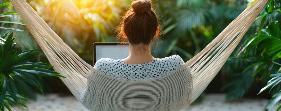 A woman relaxes in a hammock outdoors, working on a laptop surrounded by lush greenery and warm sunlight.