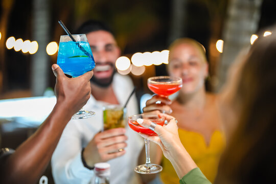 A group of young adults socializing at a lively outdoor bar at night, enjoying colorful cocktails and engaging in cheerful conversation.