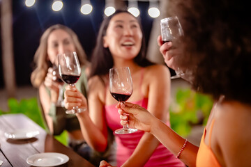 Group of friends toasting with red wine during an outdoor dinner party at night, smiling and enjoying a festive meal under string lights