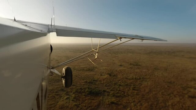 Hyperlapse of aerial wide of small plane flying over savannah with scattered shrubs and waterbody in a sunny morning in Kenya