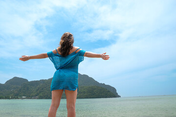 Rear view of young adult woman opening her arms contemplating wonderful island