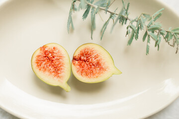 Fresh fig fruit cut in half on white plate with wattle branch