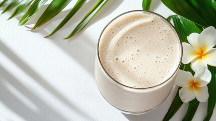 Creamy smoothie in glass surrounded by tropical leaves and flowers, evoking refreshing vibe