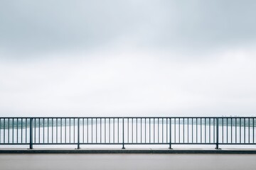 Minimalist view of a railing along a calm body of water under a cloudy sky, creating a serene atmosphere with ample copy space for text or design elements