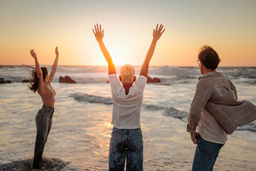 Fototapeta premium Friends raising arms enjoying golden sunset at beach