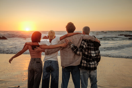 Friends embracing and admiring golden sunset on beach