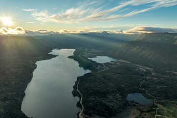 Sun rays pierce clouds over lake and smaller bodies of water surrounded by forested mountains in Patagonia under a partly cloudy sky