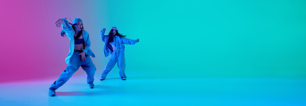 Two young dancers stretching in opposite directions under gradient cyan and pink neon lighting against gradient background with copy space. Banner. Concept of flexibility, control, and hip hop energy
