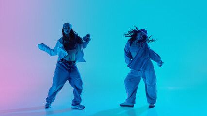 Young hip hop dancers in bright denim outfits in dance poses under pink and turquoise neon gradient...