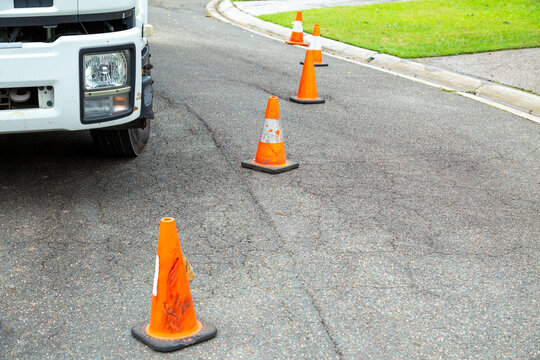 Orange traffic cones in a row blocking off work truck and suburban street.