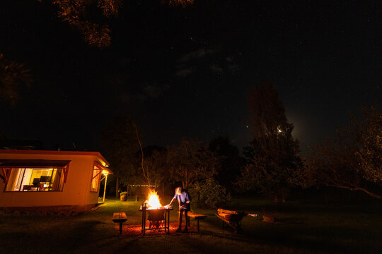 Teenage boy toasting marshmallows in backyard fire pit under starry night sky