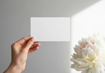 Obraz premium Woman's hand holding blank white card mockup with white peony flower 